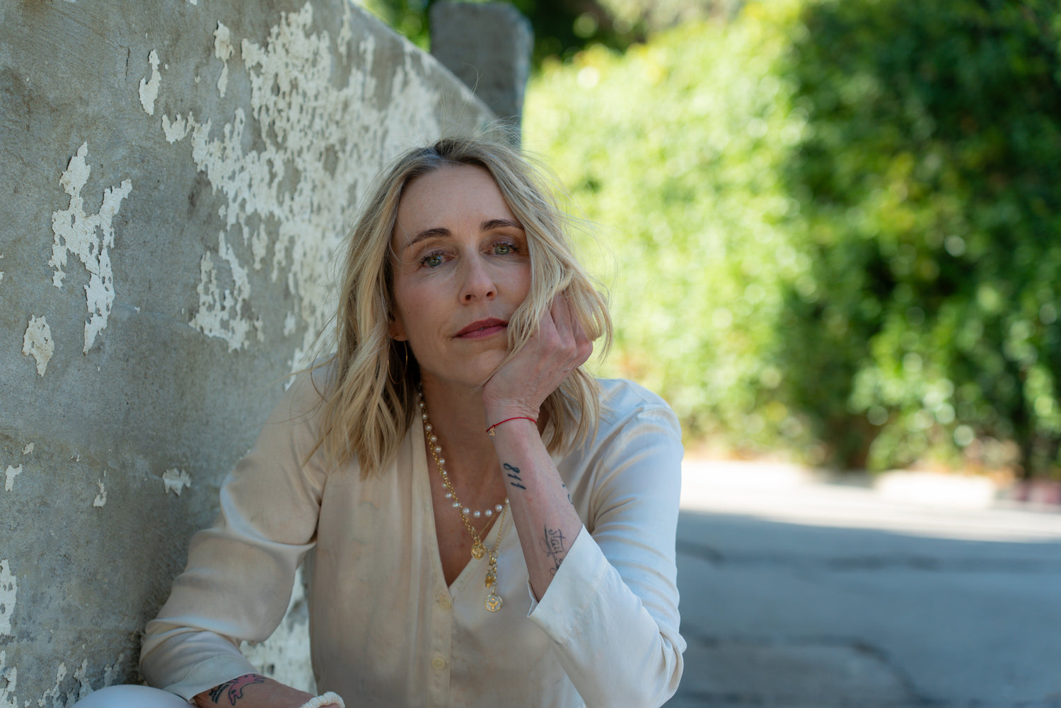 Woman leaning against a textured wall with greenery in the background