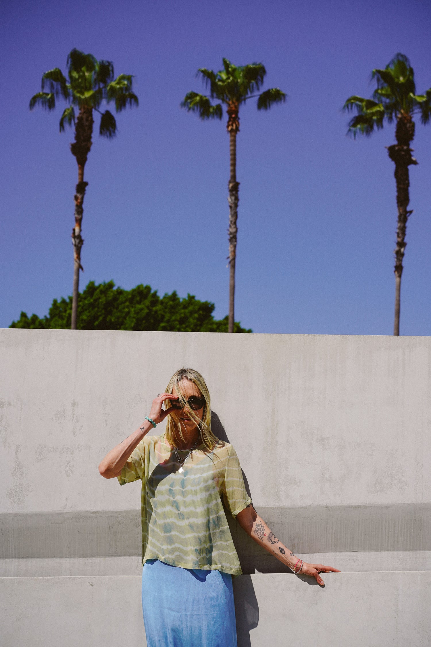 Woman standing against a wall with palm trees in the background
